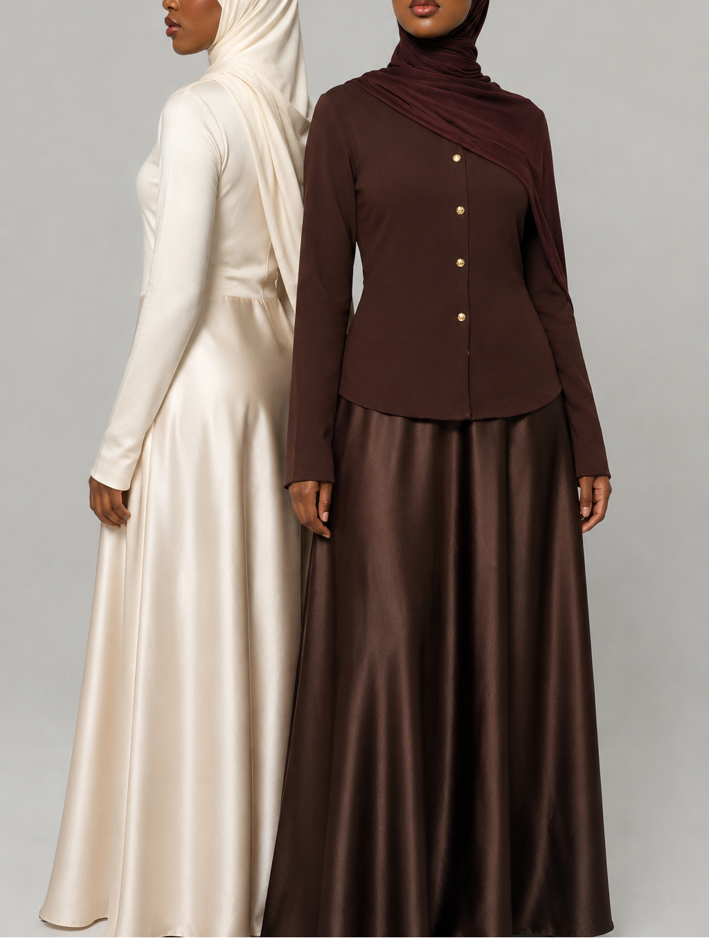 Two women wearing long, flowing dresses in white and brown on a plain background
