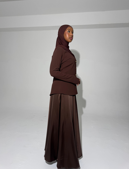 A model wearing a brown outfit with a hijab against a white background