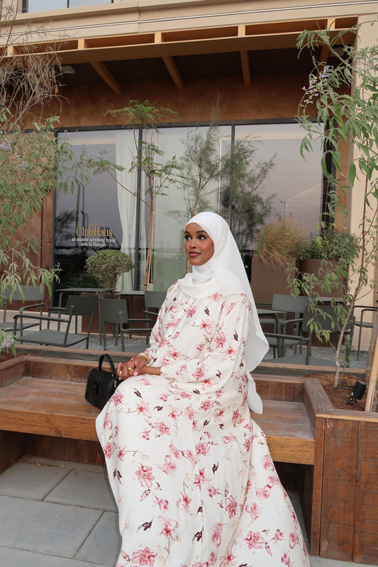 Woman wearing white floral abaya with pink print sitting outdoors – Aeko Collection